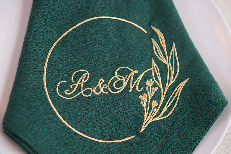 Green linen napkin with gold embroidered wedding monogram and floral wreath