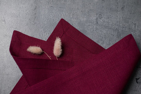 Folded plum linen napkins on concrete with dried bunny tail grass