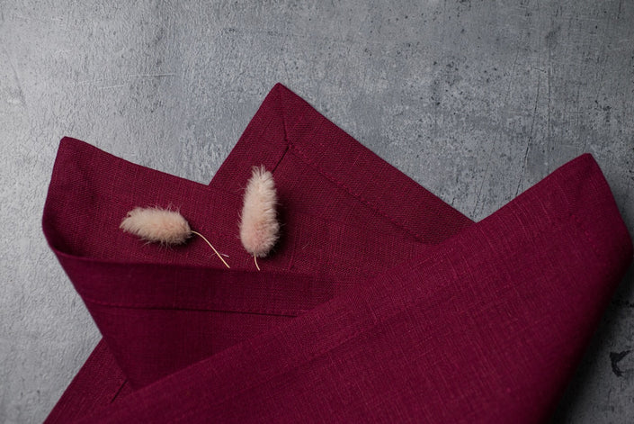Folded plum linen napkins on concrete with dried bunny tail grass