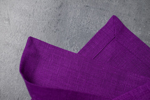 Close-up of violet organic linen with a neat mitered corner on grey concrete
