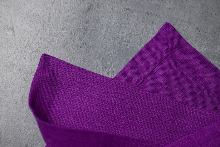 Close-up of violet organic linen with a neat mitered corner on grey concrete