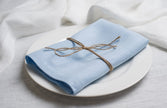Snow pale blue linen napkin tied with jute twine on a white plate, side view