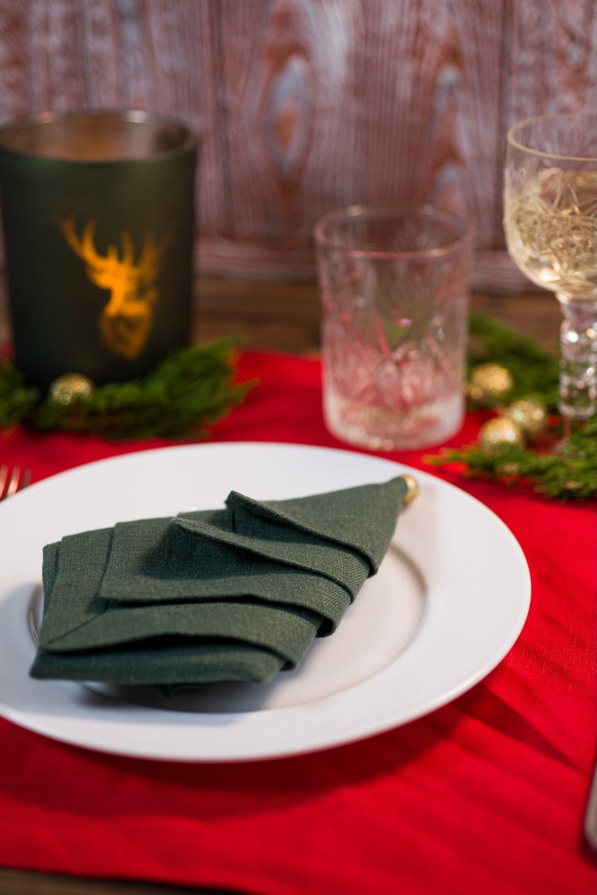 Christmas tree napkin fold in basil green organic linen with candle and crystal glasses on a festive table