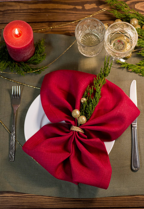 Classic red linen napkin tied into a Christmas bow with twine, gold berries and a cedar sprig