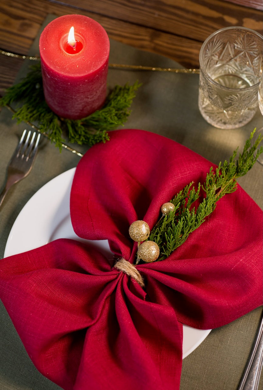 Close-up of a classic red linen napkin bow with gold berries and greenery on a Christmas place setting