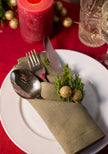 Close-up of a sage green linen napkin pocket fold with silverware and a sprig of greenery for Christmas dinner