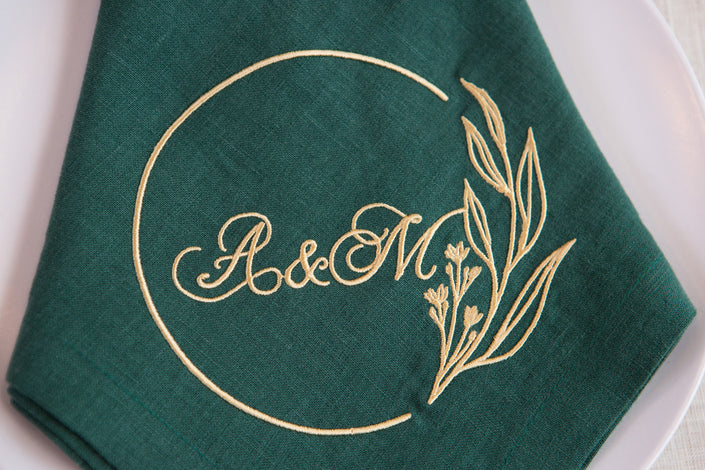 Green linen napkin with gold embroidered wedding monogram and floral wreath