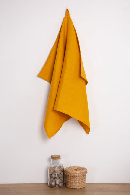 Mustard linen tea towel with a hanging loop on a wall hook