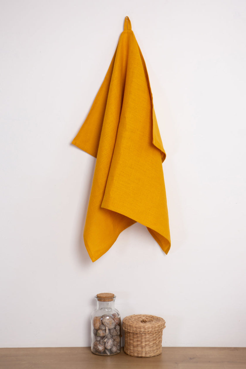 Mustard linen tea towel with a hanging loop on a wall hook