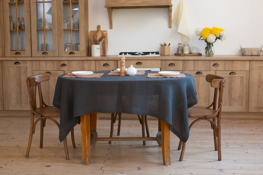 Slate (dark grey) linen tablecloth on a wooden dining table in a bright kitchen dining area.