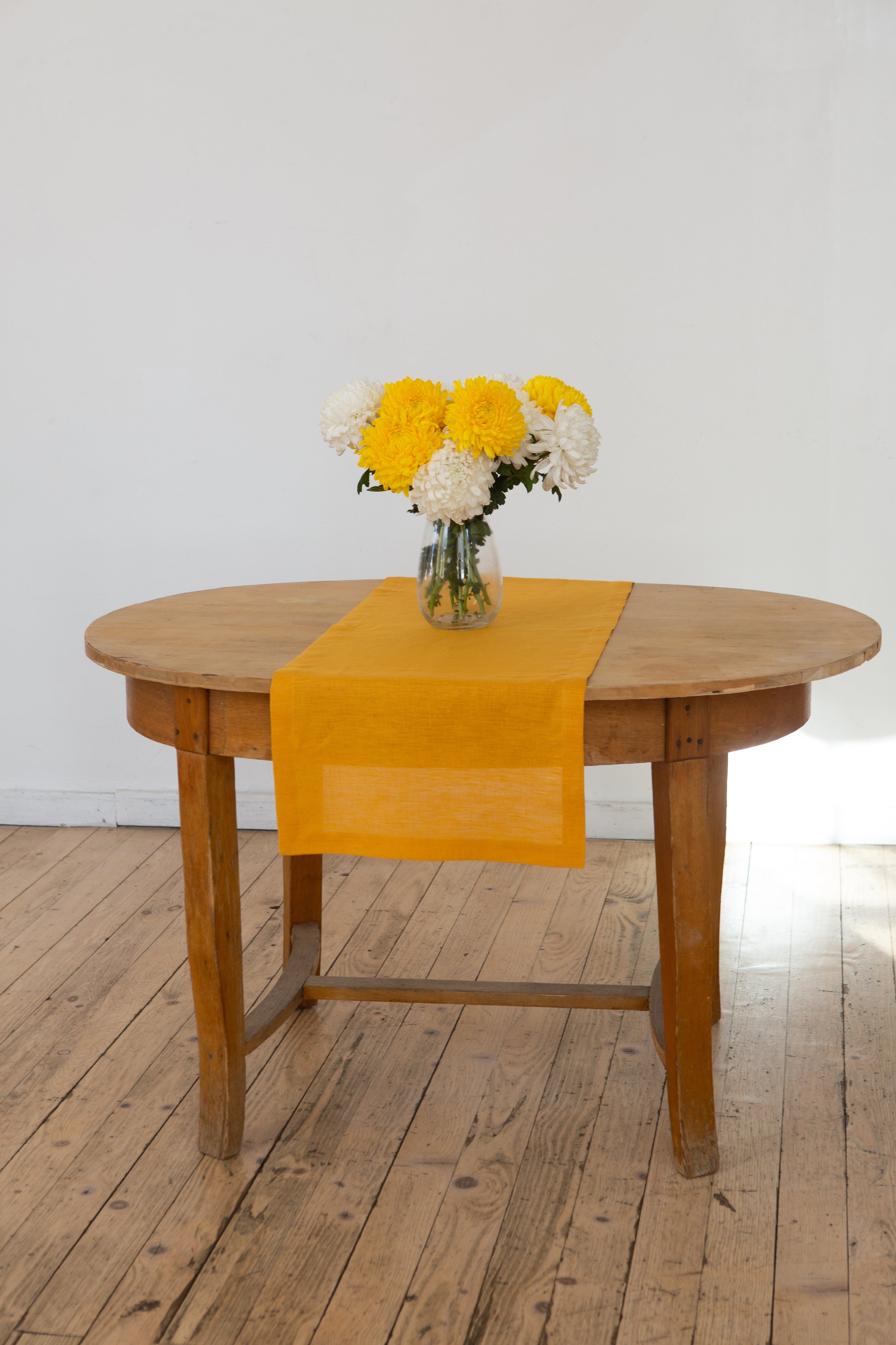 Mustard linen table runner with a vase of yellow and white chrysanthemums – fall and Thanksgiving table idea