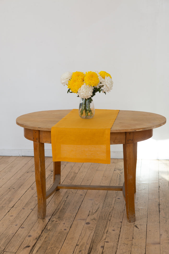 Mustard linen table runner with a vase of yellow and white chrysanthemums