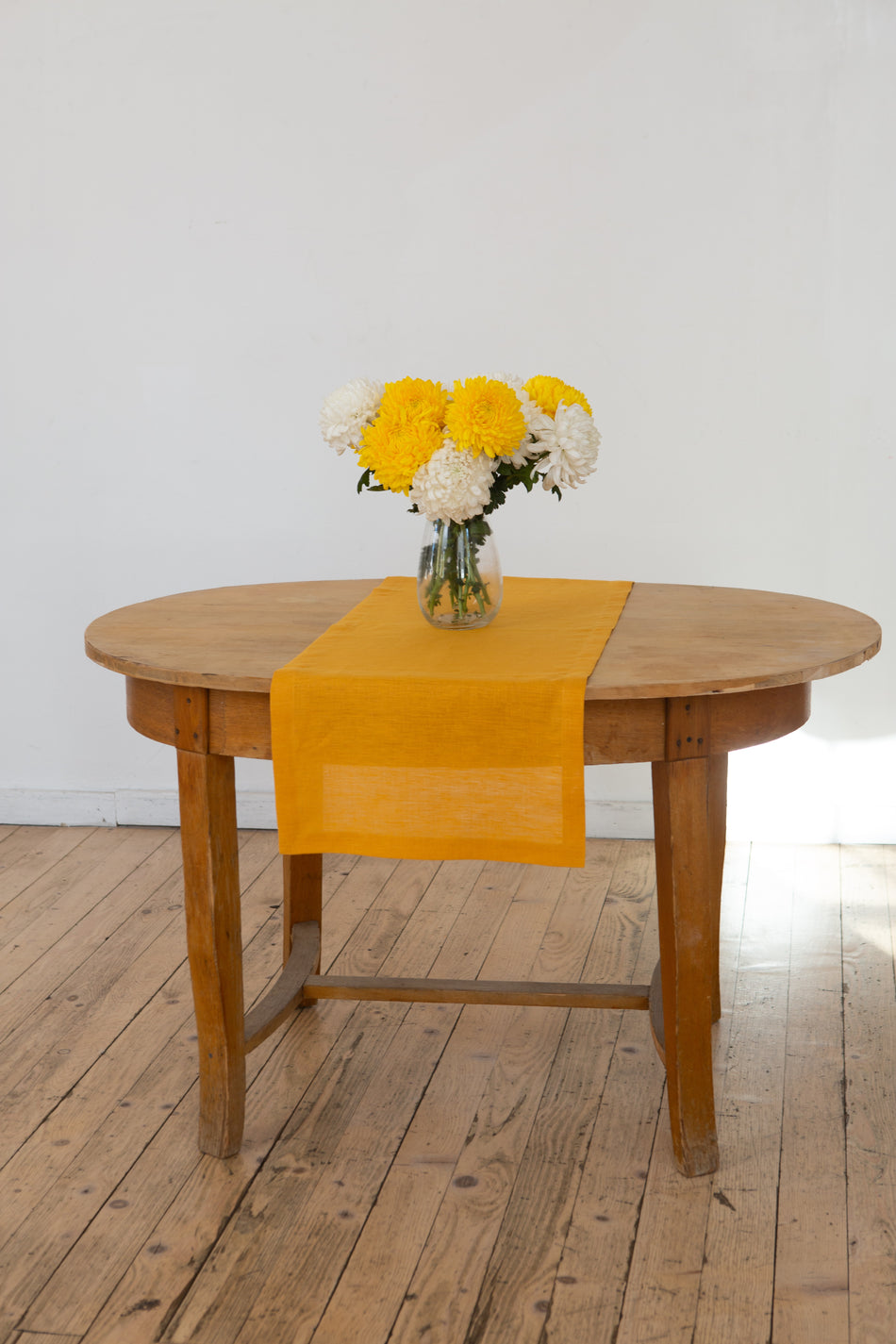Mustard linen table runner with a vase of yellow and white chrysanthemums