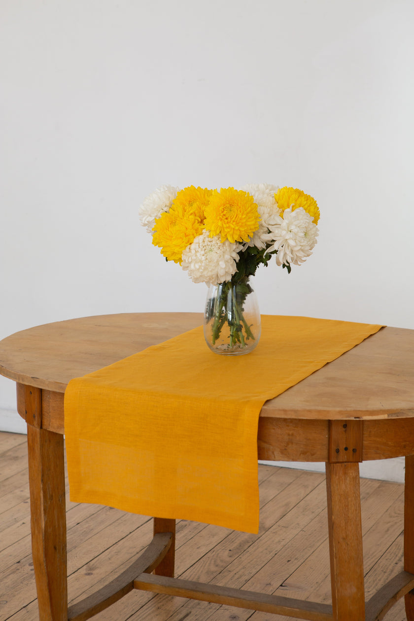 Mustard linen table runner draping over the edge of a wooden table with autumn flowers