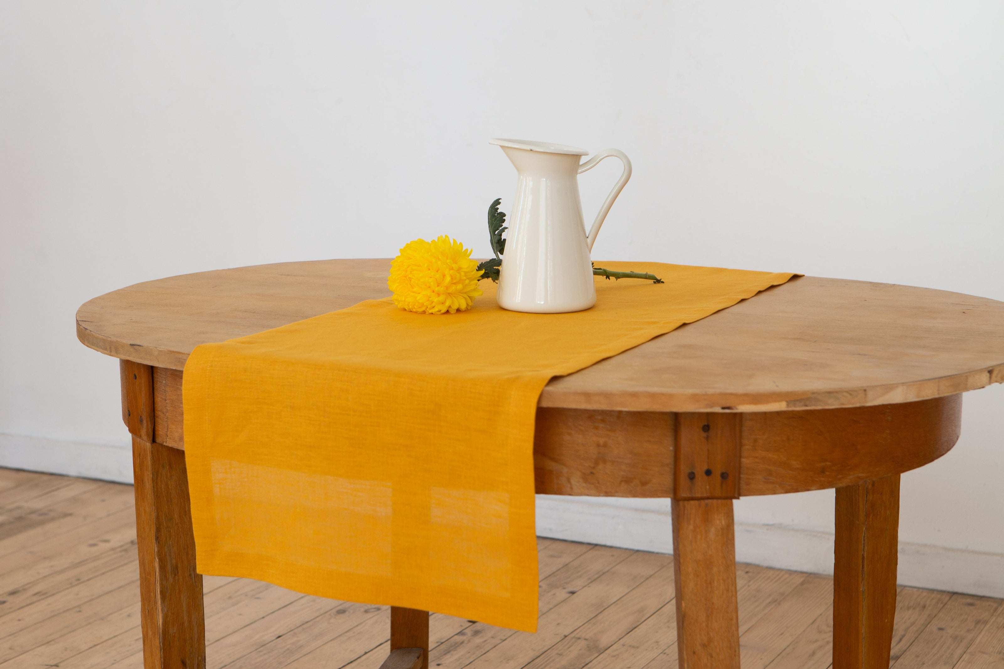Close-up of a mustard linen table runner drape with a white ceramic jug