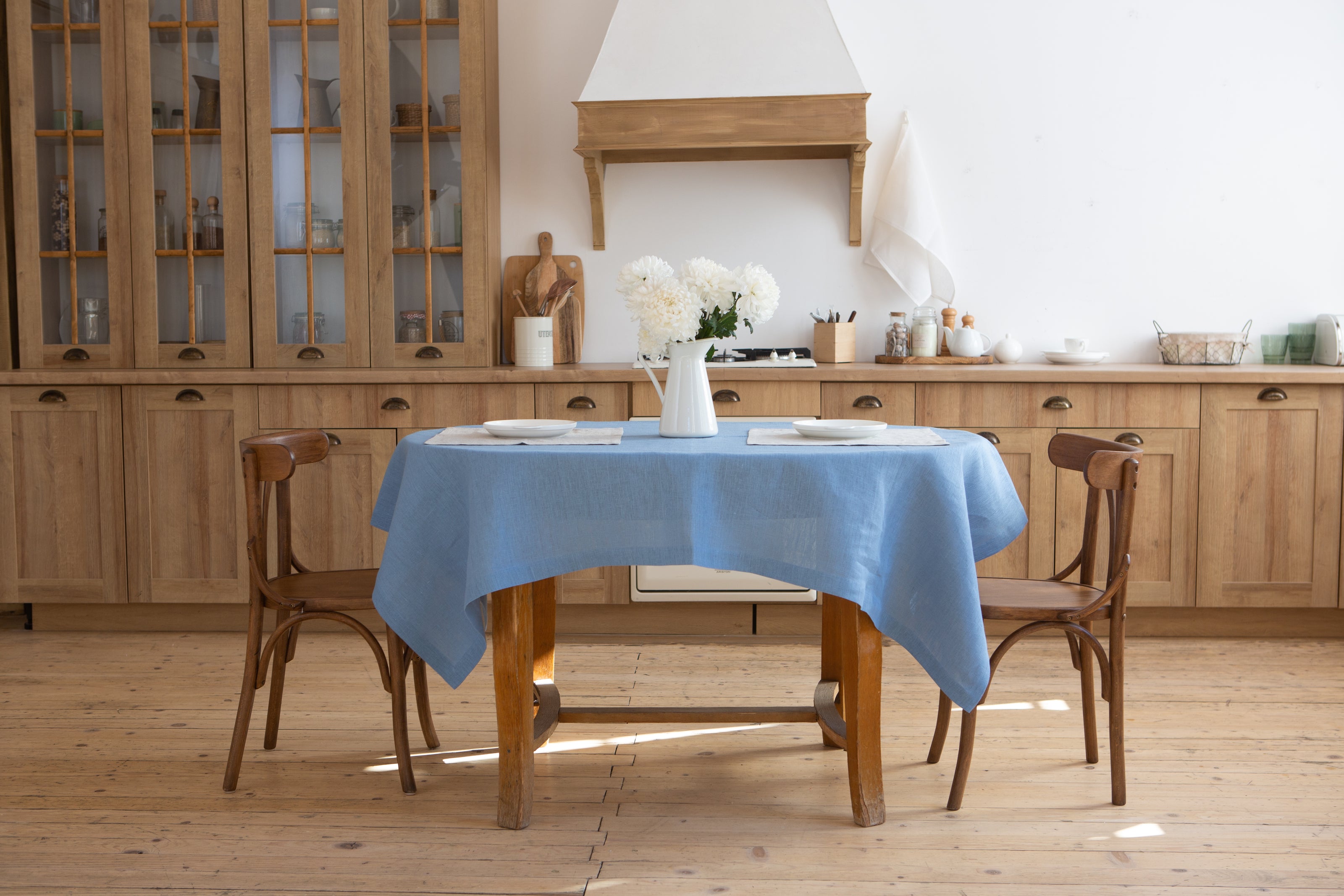 Dining area with wooden table and chairs styled with a light blue linen tablecloth in a cozy kitchen.