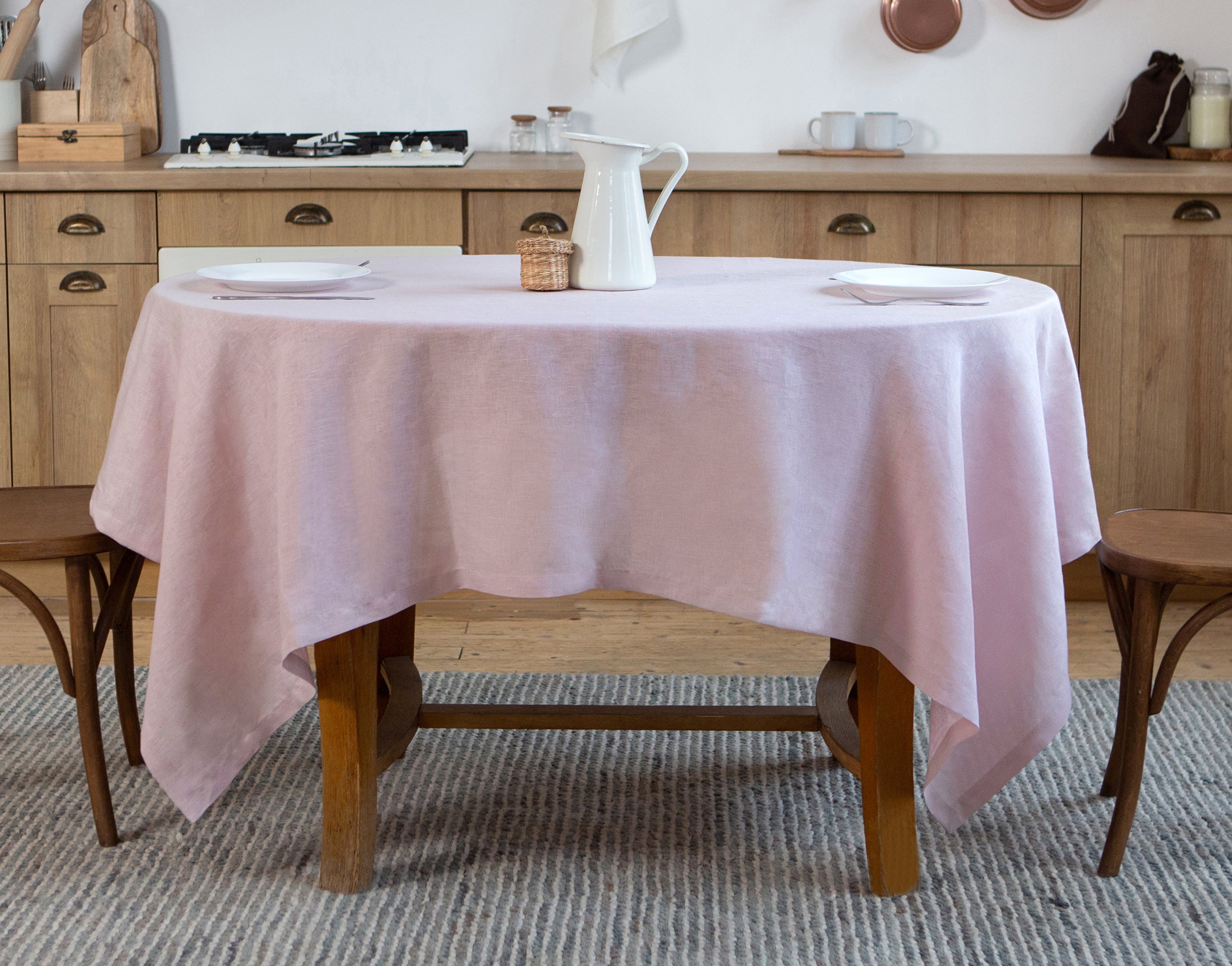 Pink linen tablecloth on a wooden dining table in a kitchen dining area with chairs.