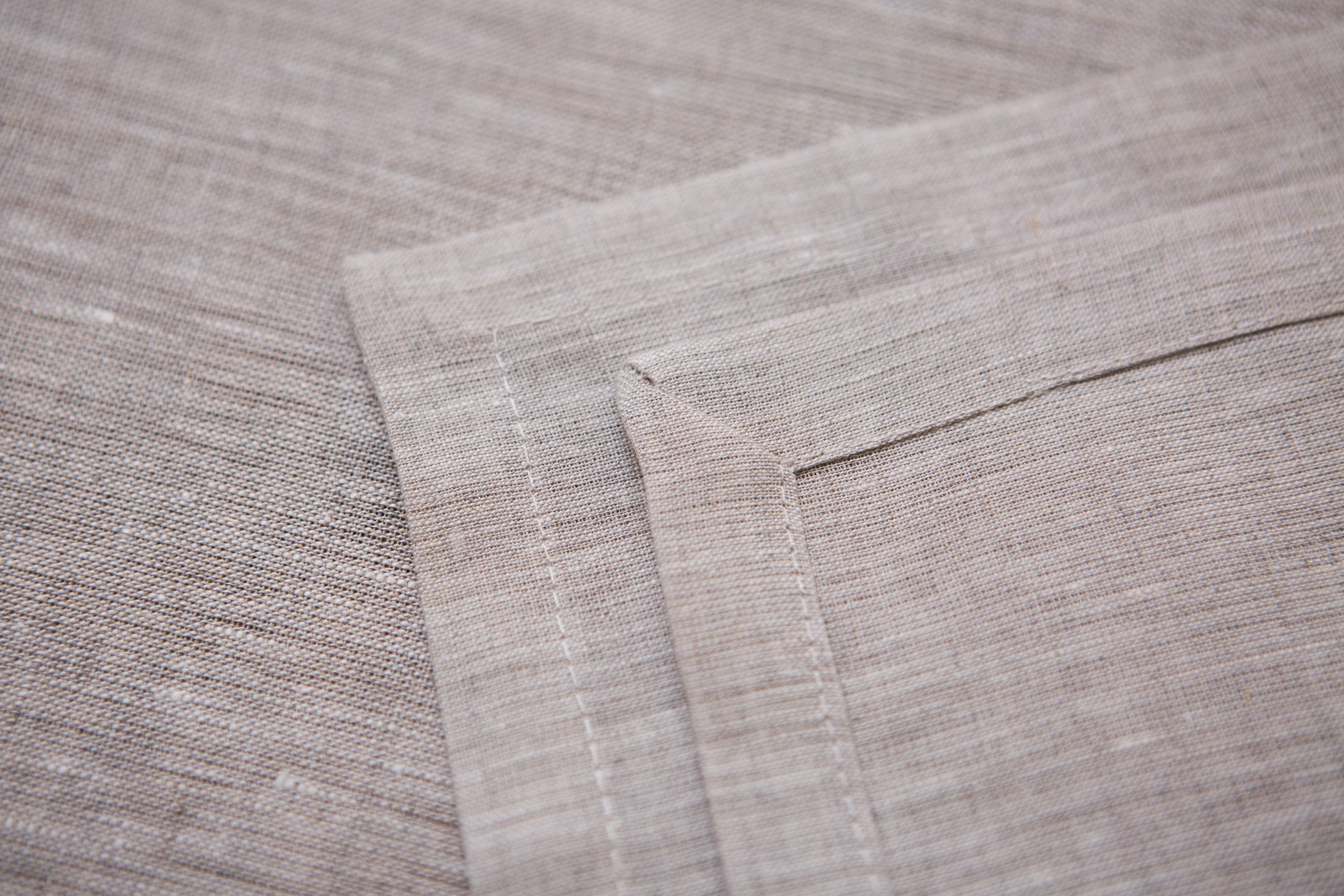 Close-up of Natural beige linen fabric showing its woven texture and mitered hem