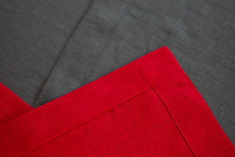 Close-up of the neatly hemmed corner of a red linen table runner
