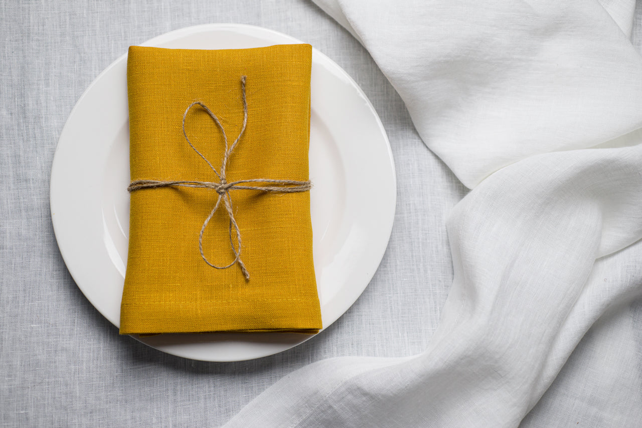 Easter yellow organic linen napkin styled with a bow on a festive spring table. Made from 100% natural linen, it adds a fresh and joyful touch to Easter brunch decor. Sustainable and reusable table textile for seasonal celebrations.