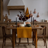 Halloween table setting with a mustard organic linen table runner, white, orange and green pumpkins, black taper candles and burgundy dahlias in a rustic kitchen – CoolLinen
