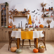 Halloween kitchen table with a natural round linen tablecloth, mustard linen table runner and napkins, black taper candles, pumpkins and paper bats – CoolLinen