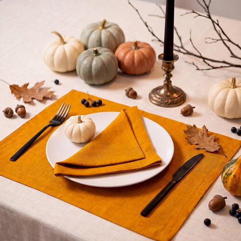 Halloween place setting with a mustard linen placemat and matching mustard linen napkin, white pumpkins, black taper candle and autumn leaves on a natural linen tablecloth – CoolLinen