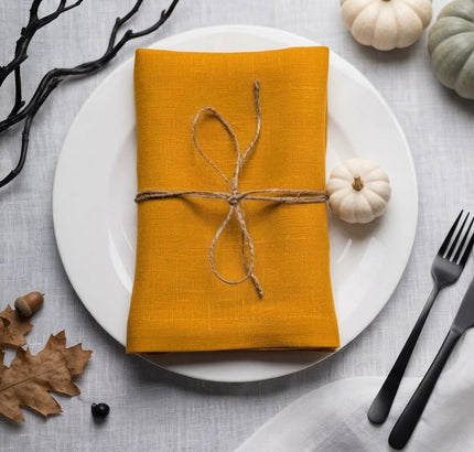 Mustard linen napkin tied with twine on a white plate beside a miniature white pumpkin for Halloween