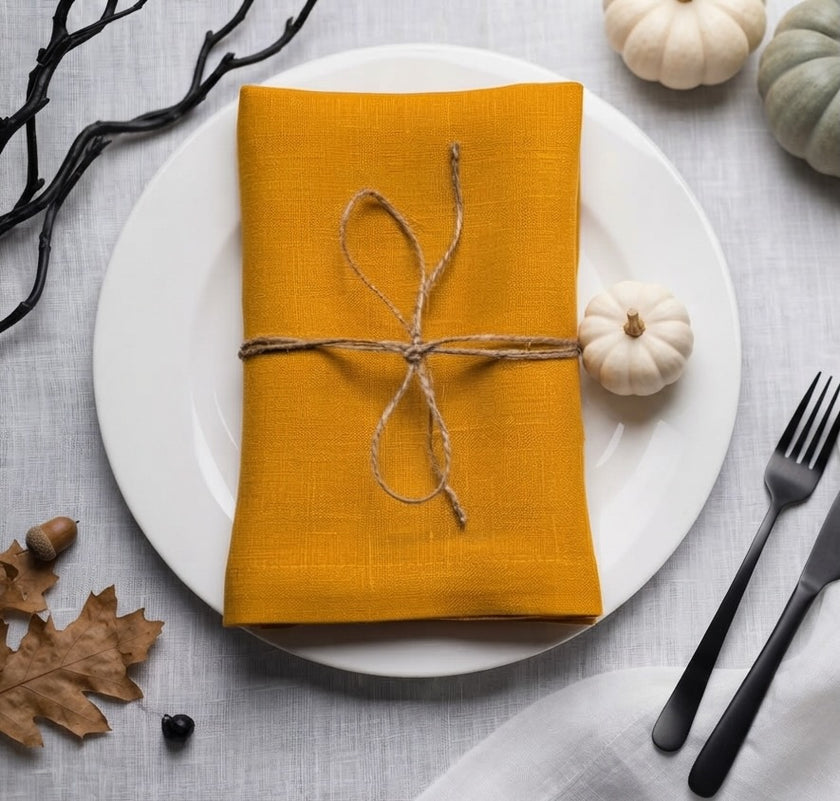 Mustard linen napkin tied with twine on a white plate beside a miniature white pumpkin for Halloween