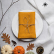 Folded mustard linen napkin with a twine bow, pumpkins and a decorative spider in a Halloween place setting