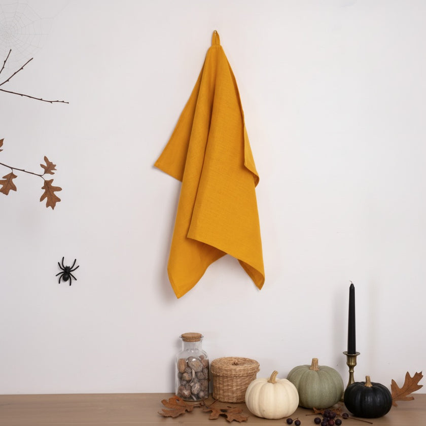 Mustard linen kitchen towel hanging above pumpkins and a black candle with decorative spiders for Halloween