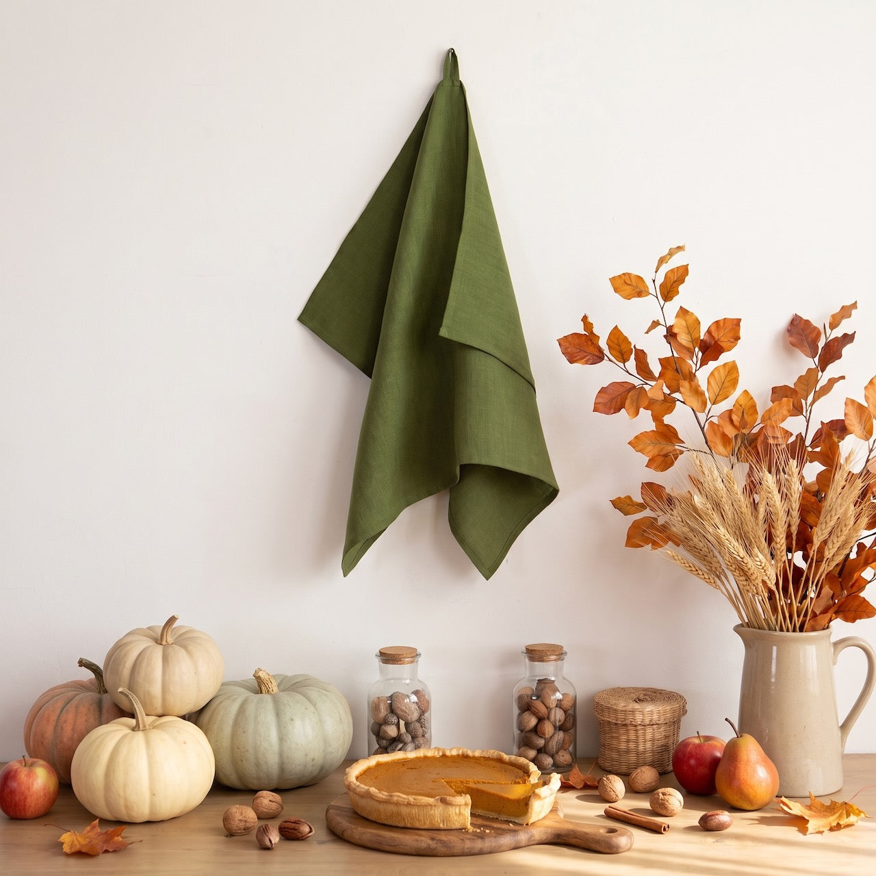Green linen kitchen towel hanging above pumpkins, pumpkin pie and autumn leaves – Thanksgiving kitchen decor – CoolLinen