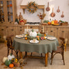 Thanksgiving table with a sage green round linen tablecloth, white and green pumpkins, taper candles and linen napkins in a rustic kitchen – CoolLinen