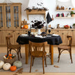 Black round linen tablecloth on a Halloween table with dark dahlias, black taper candles, pumpkins and paper bats in a rustic kitchen – CoolLinen