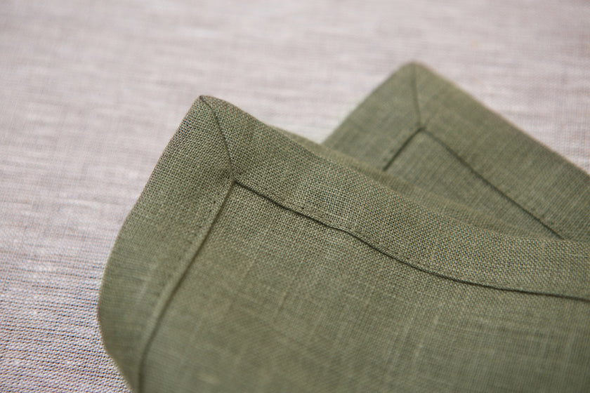 Olive green linen napkins with mitered corners, close-up