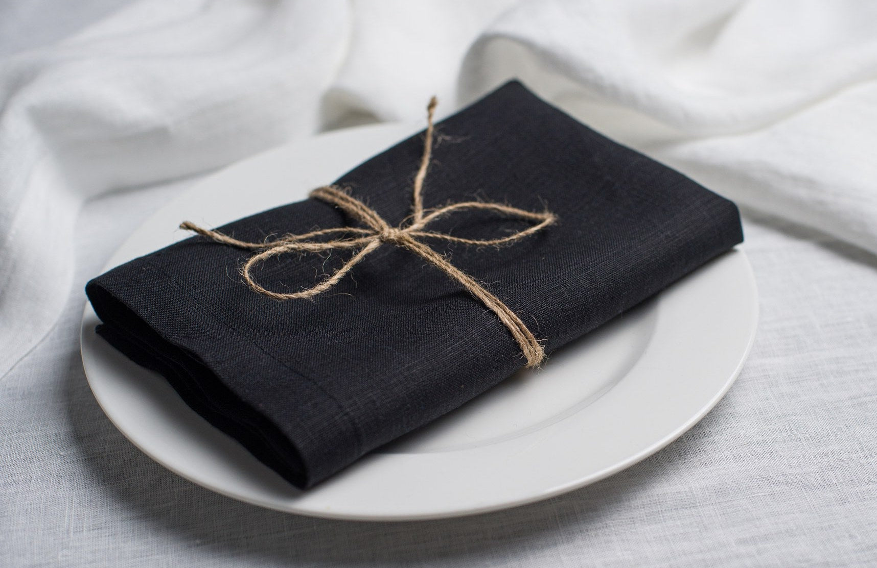 Black linen napkin tied with jute twine on a white plate, side view