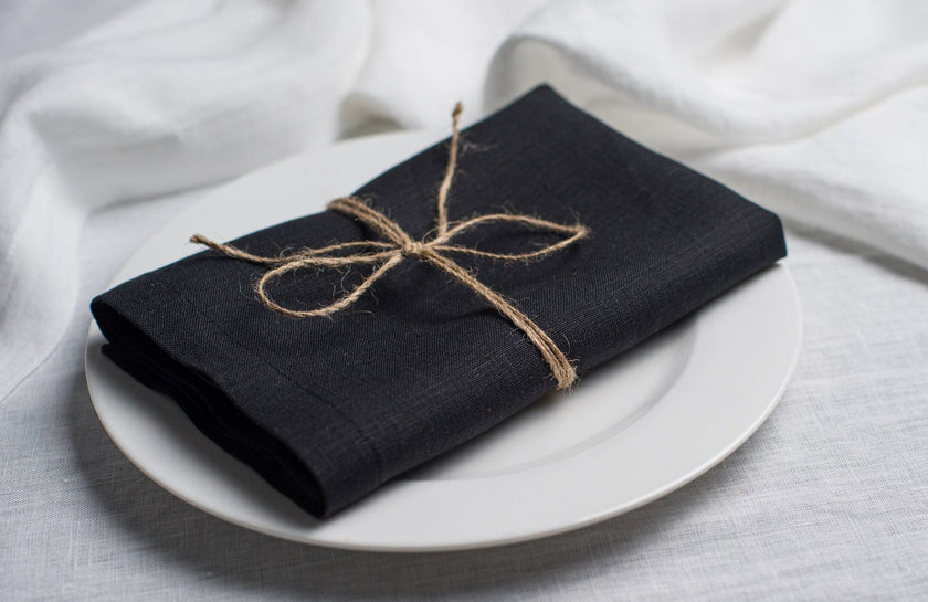 Black linen napkin tied with jute twine on a white plate, side view