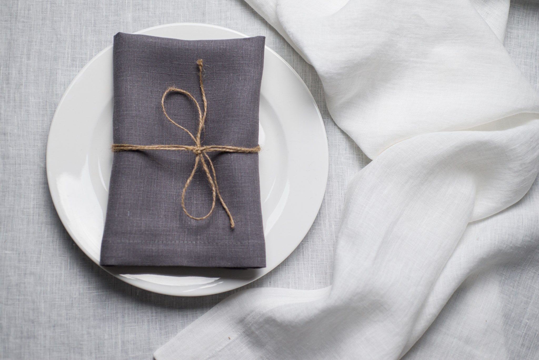 Grey linen napkin tied with jute twine on a white plate