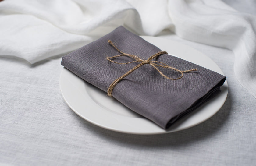 Grey linen napkin tied with jute twine on a white plate, side view