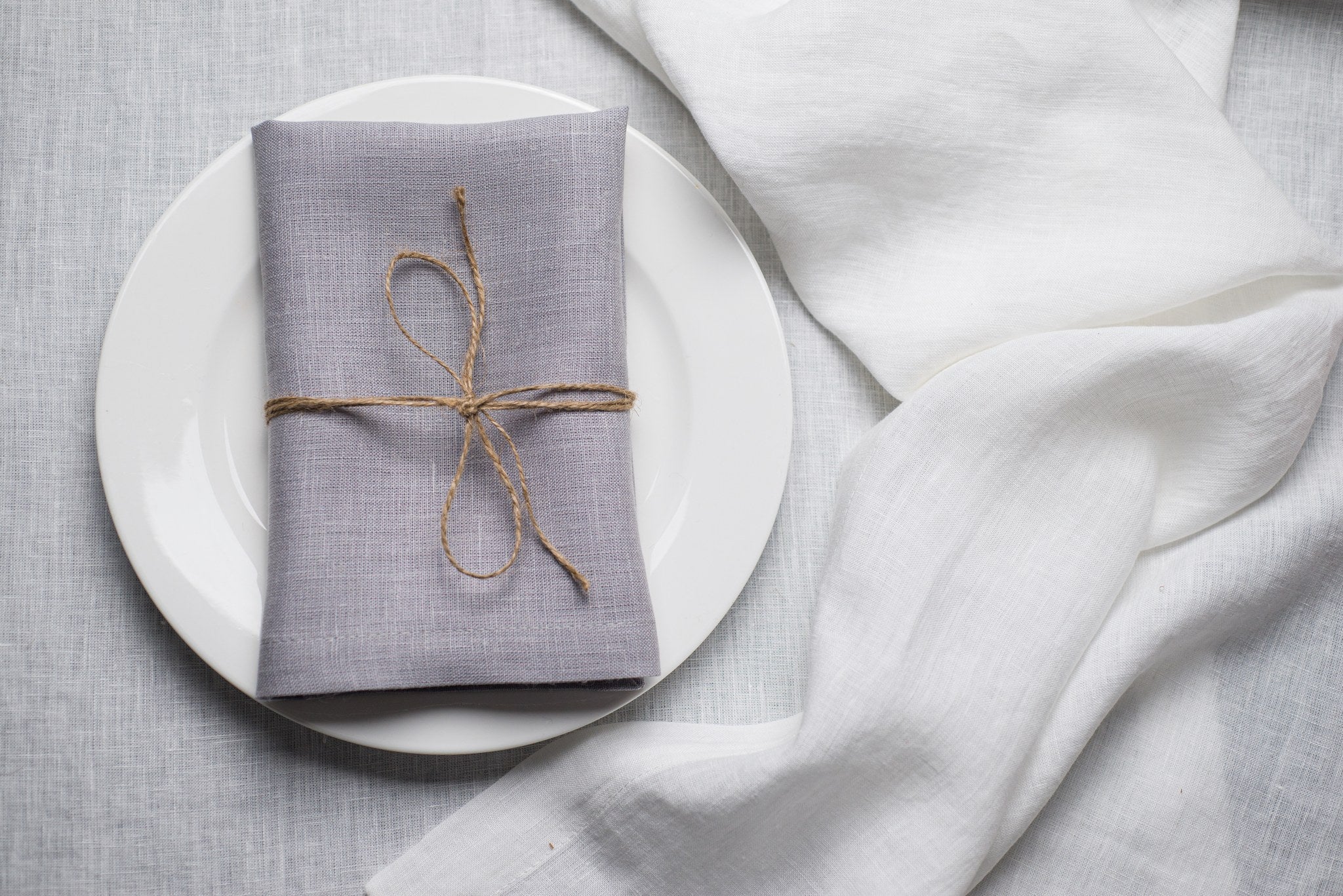 Light Grey linen napkin tied with jute twine on a white plate