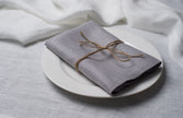 Light Grey linen napkin tied with jute twine on a white plate, side view
