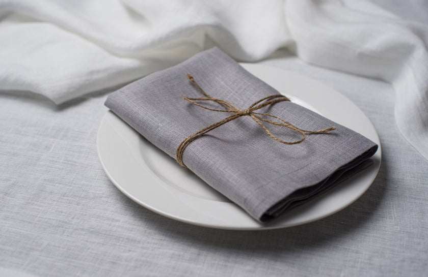 Light Grey linen napkin tied with jute twine on a white plate, side view