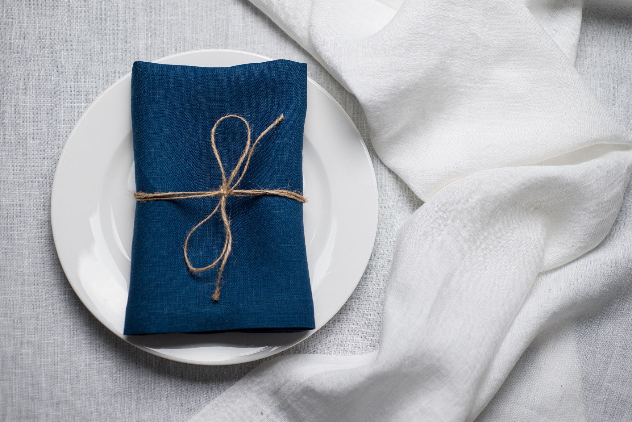 Blue linen napkin tied with jute twine on a white plate