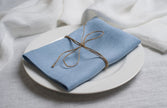 Sky linen napkin tied with jute twine on a white plate, side view