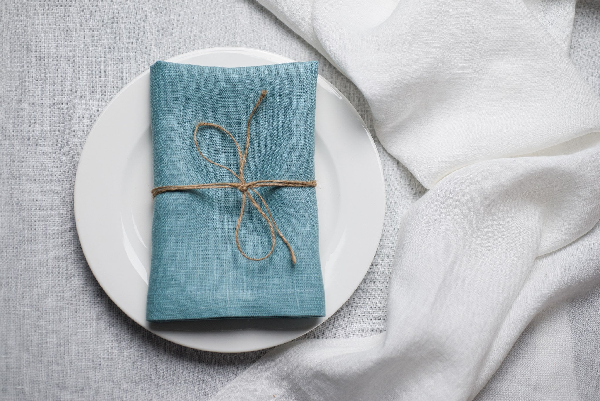 Teal linen napkin tied with jute twine on a white plate