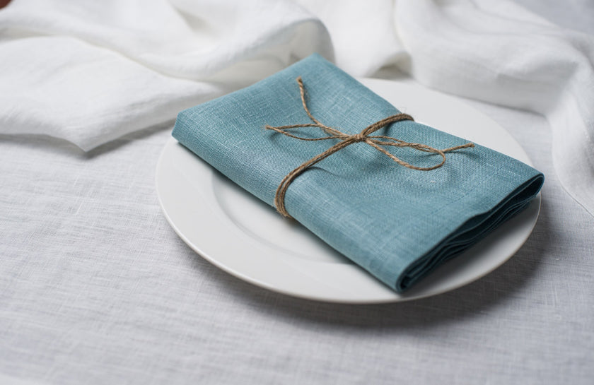 Teal linen napkin tied with jute twine on a white plate, side view