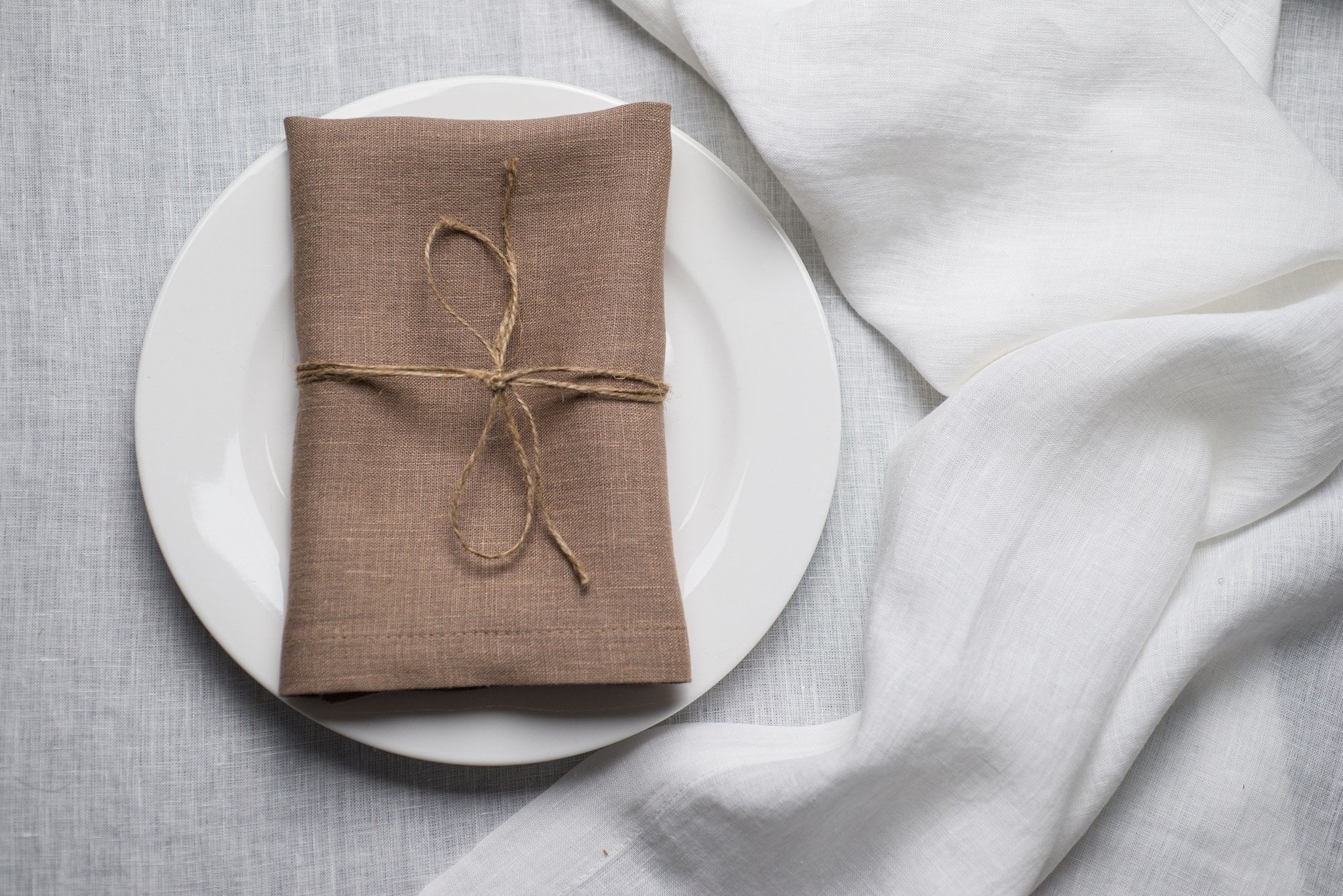 Oat linen napkin tied with jute twine on a white plate
