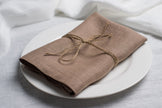 Oat linen napkin tied with jute twine on a white plate, side view