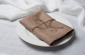Oat linen napkin tied with jute twine on a white plate, side view