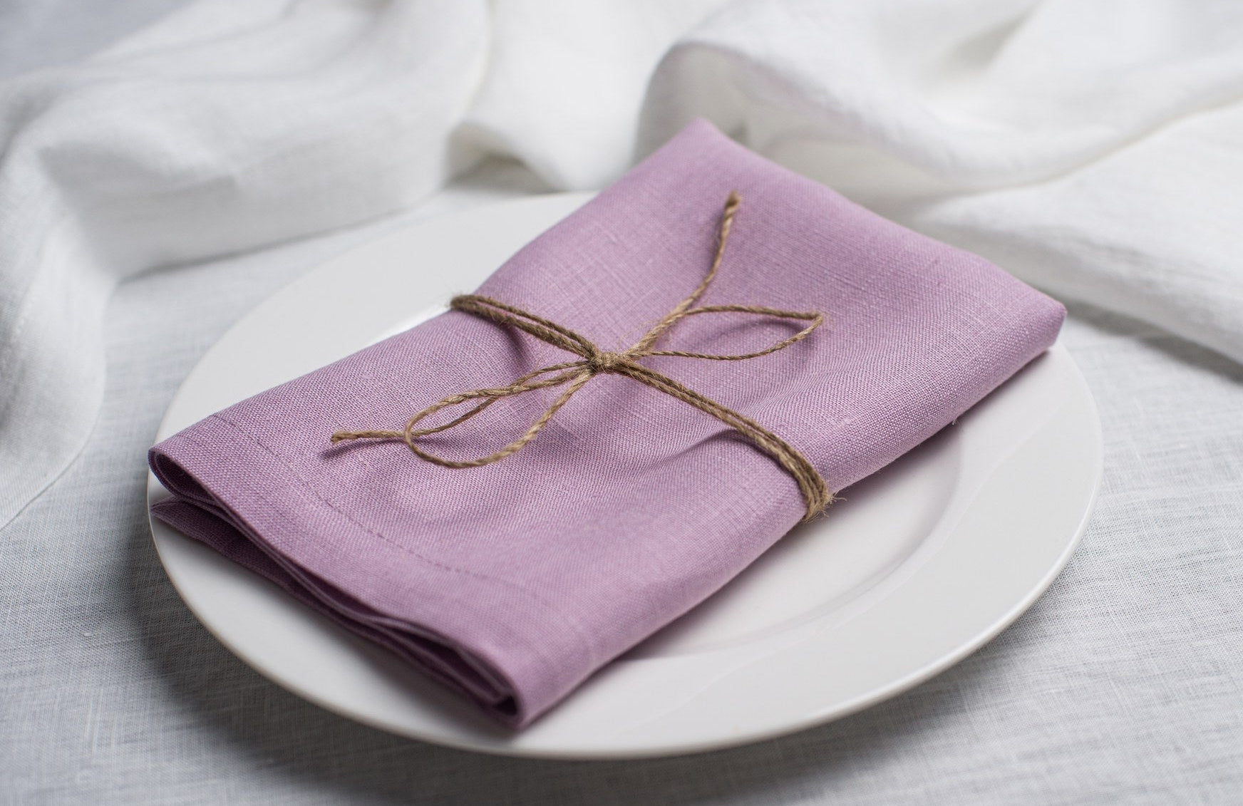 Lavender linen napkin tied with jute twine on a white plate, side view
